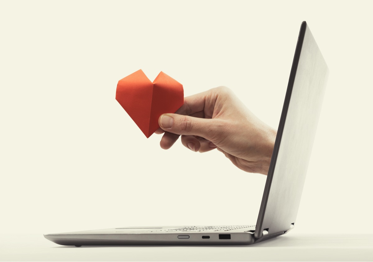 Hand coming out of laptop screen holding a heart